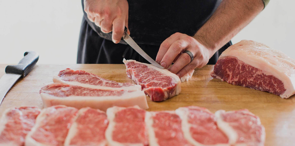 Porter Road butcher hand-cutting New York Strip steaks on a butcher block